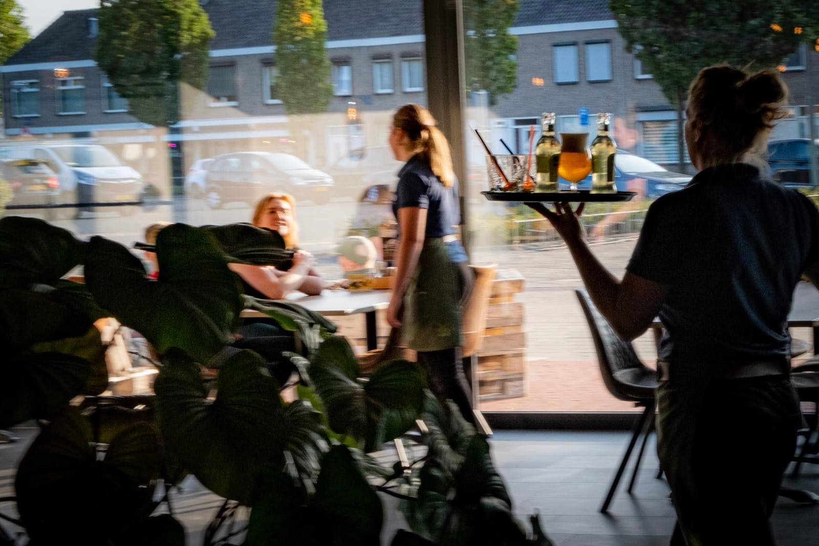 Bediening loopt met een dienblad drankjes langs de ramen